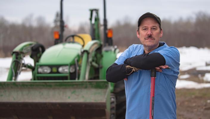 Jim Golen standing in a field with his backhoe behind him.