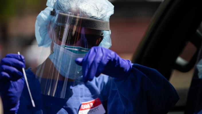 person with plastic face shield, gloves, and covid test swab