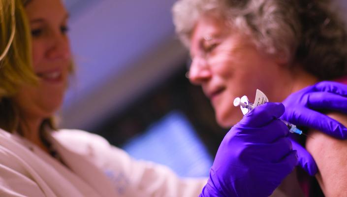 a nurse wearing purple gloves prepares to vaccinate an older adult woman