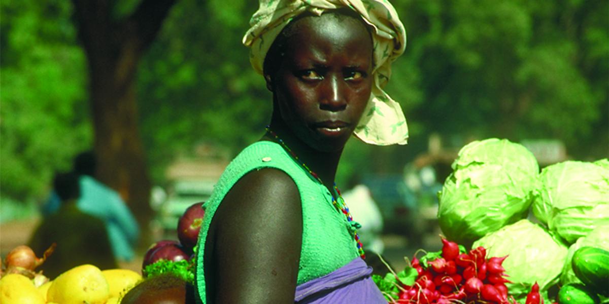 An African woman in a produce market carries her baby in a wrap on her back