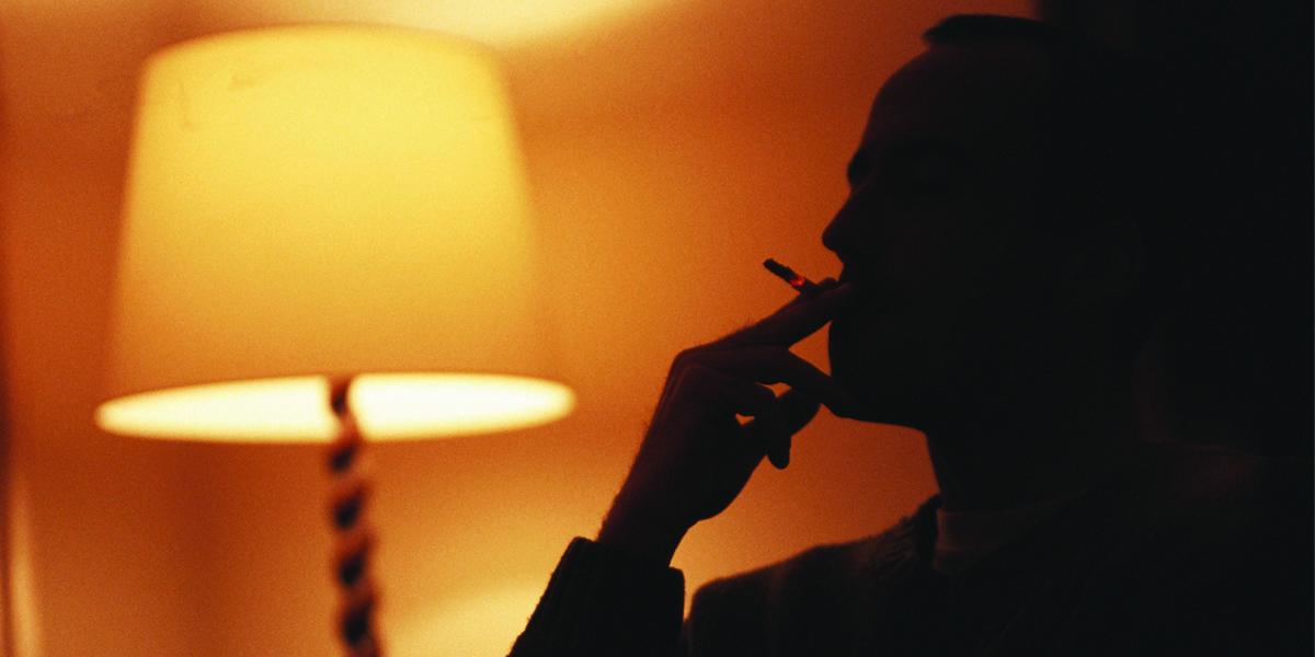 silhouette of a person smoking in the light of a living room lamp