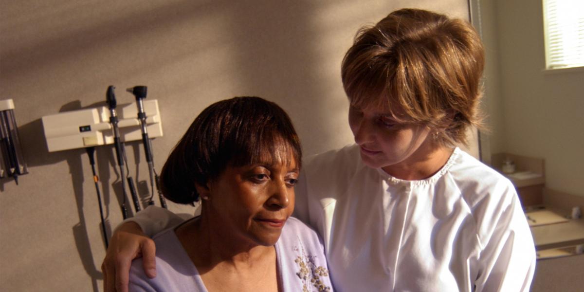 a doctor stands next to a patient's beside with her arm around the patient's soldier