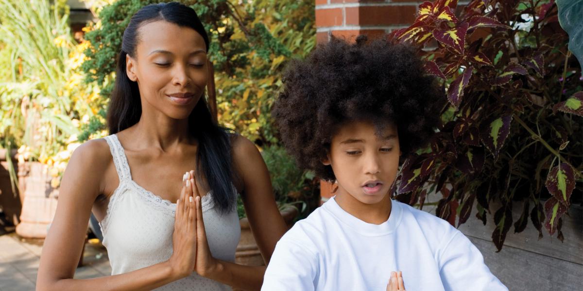 A mother and son sit with their eyes closed and their palms pressed together