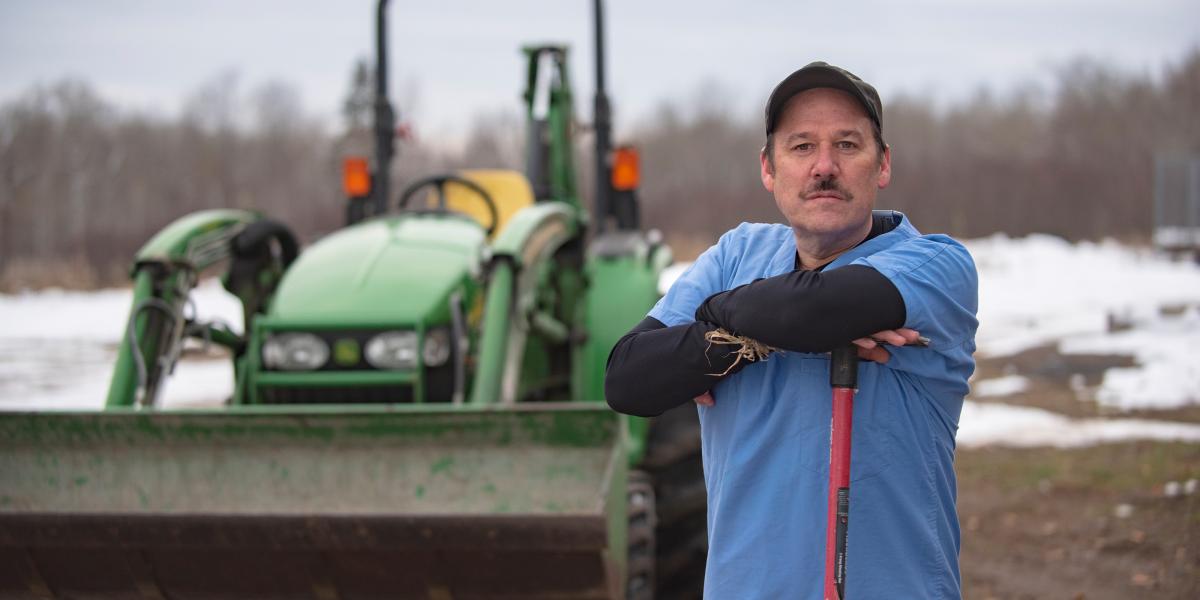 Jim Golen standing in a field with his backhoe behind him.