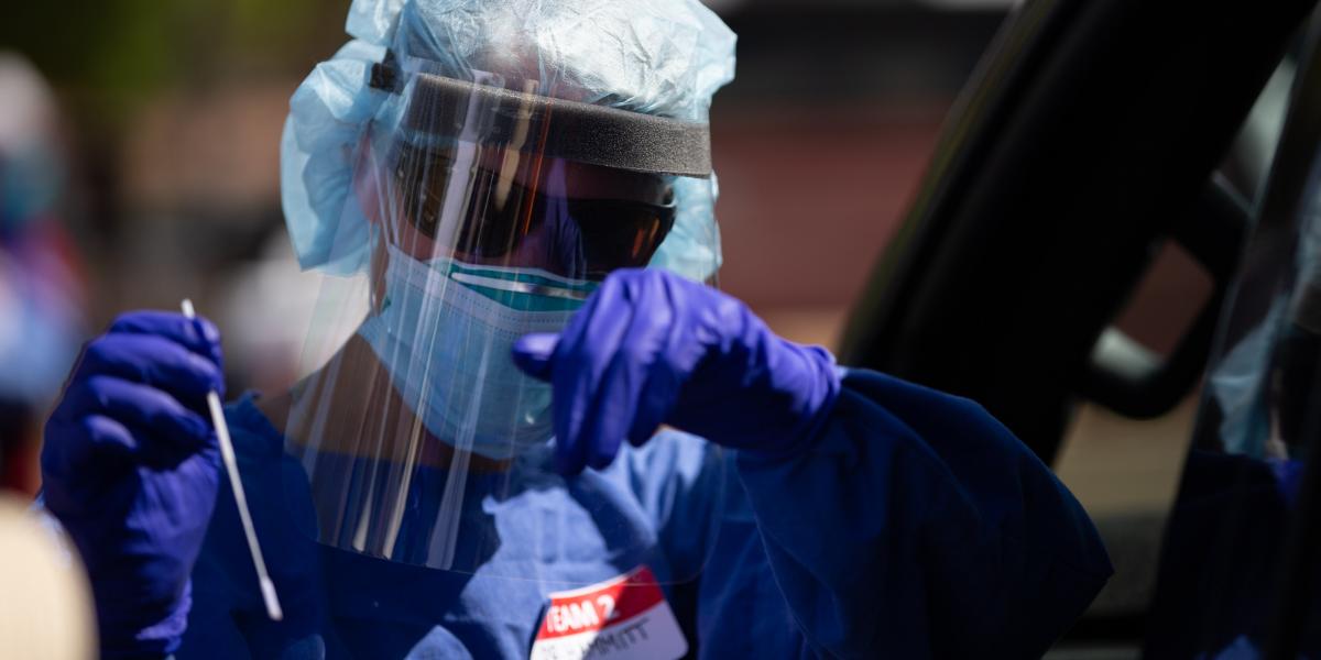 person with plastic face shield, gloves, and covid test swab