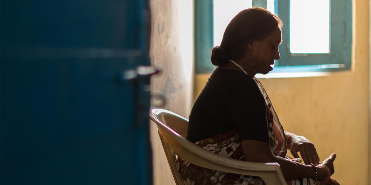 an Indian woman in a striped and floral sari  sits in a plastic chair; she faces to the right