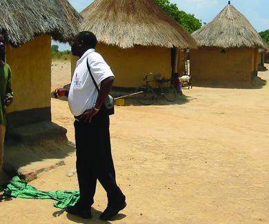 a CREATE worker talks with a community member outside a mud and thatch house