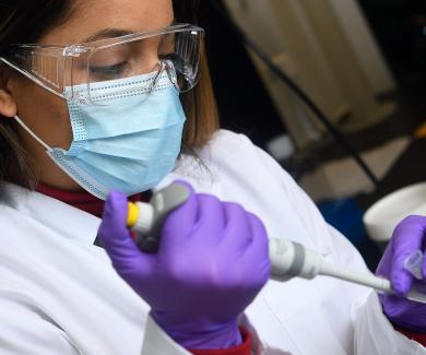 Woman wearing goggles, mask, and gloves, working with laboratory equipment