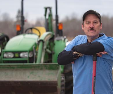 Jim Golen standing in a field with his backhoe behind him.