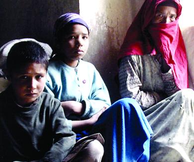 An Afghan woman in a headscarf huddles with her two grandchildren on the floor