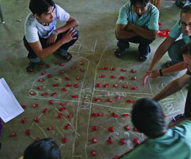 Luke Mullany and Kate Teela squat on the floor as they teach interval sampling to Burmese surveyors, using red candy packets on a chalked diagram